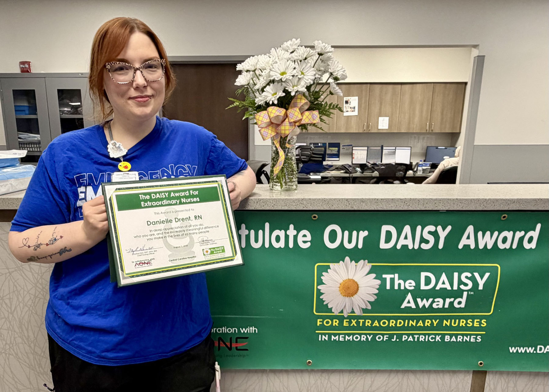 Danielle Drent standing in front of Daisy Award banner holding a Daisy Award certificate